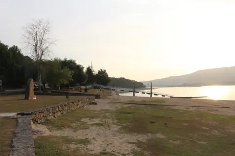 Un tranquilo atardecer en la playa fluvial o corgo, con un muelle y vegetación verde.