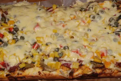 Pyszna pizza na grubym cieście z warzywami i roztopionym serem.