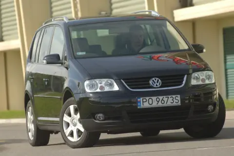 Czarny VW Touran z przodu, widoczne reflektory i żarówki. Kierowca za kierownicą.