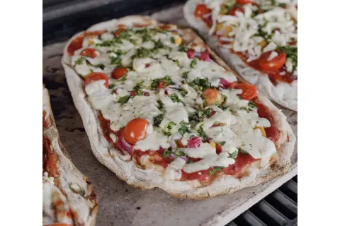 Dwie pizze na kamieniu, z pomidorkami i serem. Dowiedz się, jak przełożyć pizzę na kamień bez łopatki, by uzyskać idealnie chrupiący spód.