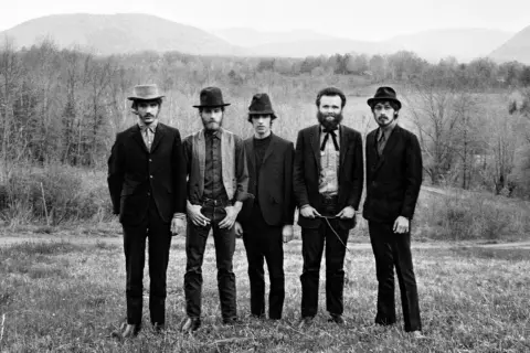 The Band, who wrote "The Weight," pose in a field with mountains in the background.