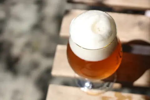 Ein Glas Bier mit viel Schaum steht auf Holzplanken. Vorsicht bei der Einnahme von Letrozol und Alkohol.