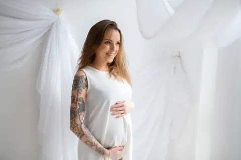 Uśmiechnięta ciężarna kobieta z tatuażem na ramieniu. Czy można zrobić tatuaż w ciąży? To pytanie nurtuje wiele przyszłych mam.