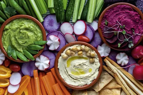 Bunte Auswahl an Dip-Rezepten: cremiger Hummus, grüner Avocado-Dip und Rote-Bete-Dip mit frischem Gemüse und Brot.