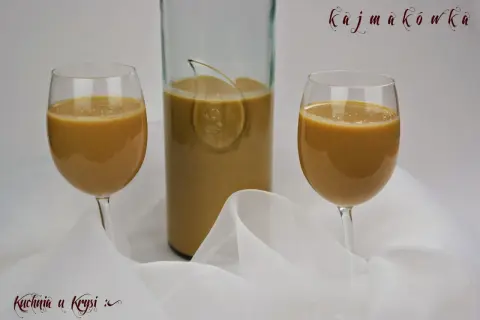 Kajmakówka, czyli likier krówkowy z masy kajmakowej, w kieliszkach i butelce, na tle białej tkaniny.