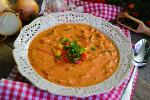 Aksamitna zupa gyros z kurczakiem i pieczarkami, udekorowana kolorową papryką i natką pietruszki. Obok leżą cebule i czosnek.