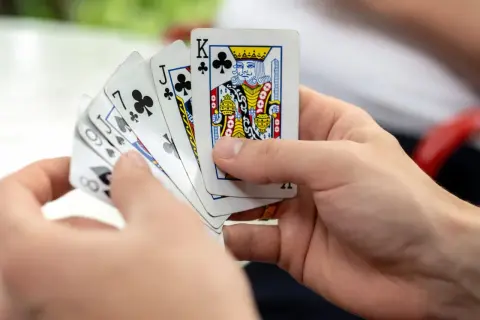 Ręce trzymają karty do gry, wśród nich król trefl. Czas na grę w kuku!
