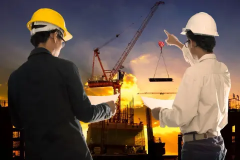 Ingegneri supervisionano un cantiere edile al tramonto, garantendo la sicurezza. Gru solleva materiale.