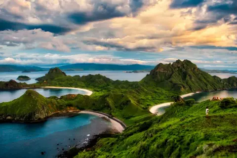 Grüne Hügel und weiße Sandstrände im Komodo Nationalpark, Indonesien. Ein einsamer Wanderer genießt die atemberaubende Aussicht auf das Meer.