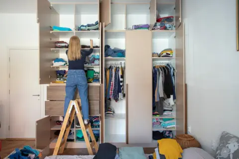 Mädchen auf Trittleiter sortiert Kleidung in einem großen Kleiderschrank, um **Stauraum schaffen**.