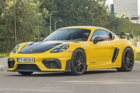 Żółty Porsche Cayman GT4 RS z czarną maską i spojlerem, gotowy do jazdy po miejskich ulicach.