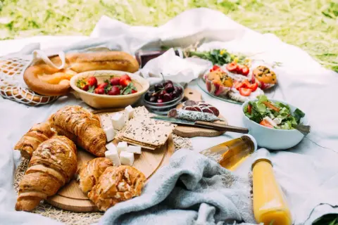 Pyszne jedzenie na piknik: świeże croissanty, bagietka, truskawki, wiśnie, sałatka, kiełbasa i napoje.
