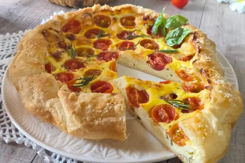 Une quiche ricotta aux tomates cerises et romarin, garnie de graines de sésame, sur une assiette blanche.