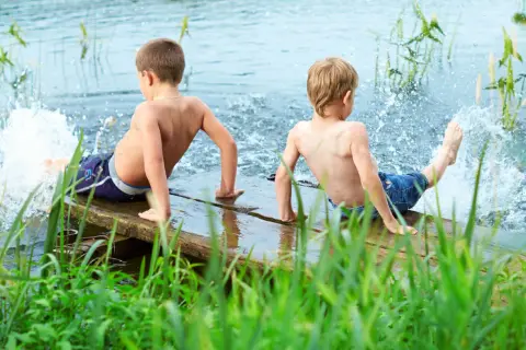 Two boys enjoy parallel play, splashing water from a wooden dock.