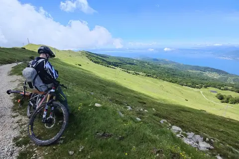 Ciclista con mountain bike ammira il panorama del lago di Garda dal Monte Baldo.