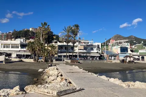 Paseo marítimo en la playa pedregalejo como llegar. Palmeras, restaurantes y montañas al fondo bajo un cielo azul.
