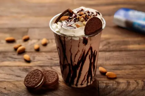 Un délicieux milkshake vegan au chocolat, garni de crème, d'amandes et de biscuits, sur fond de bois.