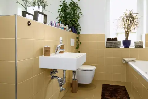 Bagno moderno con piastrelle color sabbia, lavabo sospeso, WC e vasca. Un'idea per dipingere piastrelle bagno con un tocco di calore.