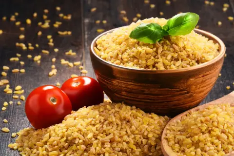 Miseczka kaszy bulgur, pomidory i drewniana łyżka. Czy kasza bulgur jest zdrowa? Tak, to bogactwo błonnika i witamin.
