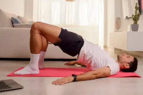 Uomo esegue esercizi di Kegel a casa, seguendo un tutorial su laptop.