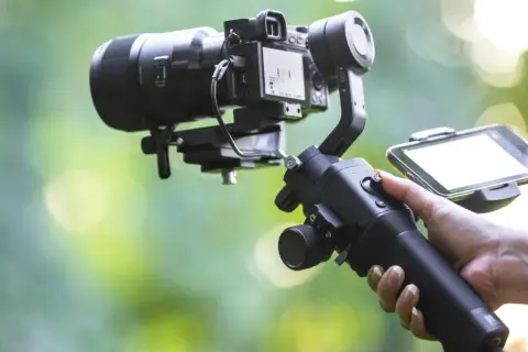 Ręka trzymająca stabilizator do kamery, czyli co to gimbal. Umożliwia płynne nagrywanie filmów.