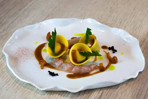 Trois raviolis italiens dorés, garniture de crevettes, champignons et sauce brune sur une assiette blanche ondulée.