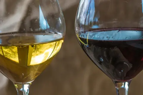 Dwa kieliszki wina, białe i czerwone. Czerwone wino może mieć skutki uboczne, ale oba napoje kuszą smakiem.