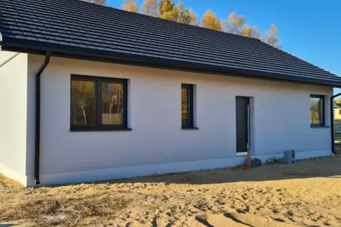 Nowy dom w stanie surowym zamkniętym z szarym dachem i oknami, otoczony piaskiem.