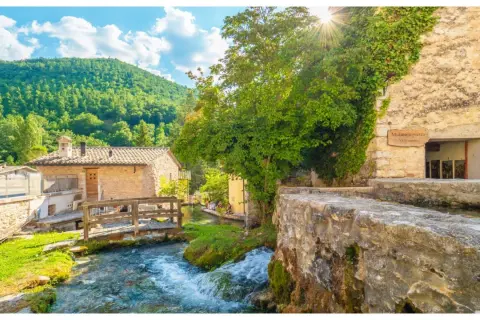 Un ruscello attraversa un borgo umbro con case in pietra e vegetazione lussureggiante. Una cartina ideale per scoprire i borghi dell'Umbria.