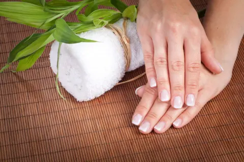 Delikatne dłonie z francuskim manicure, biały ręcznik i zielone liście bambusa. Czy to jest manicure japoński?