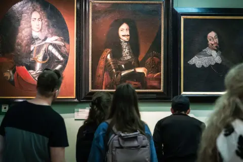 Zwiedzający podziwiają portrety w muzeum sztuki Wrocław. Widać barokowe stroje i peruki.