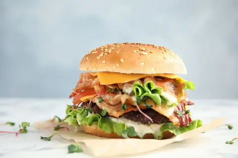 Soczysty burger z wołowiny z bekonem, serem i warzywami na jasnym tle.