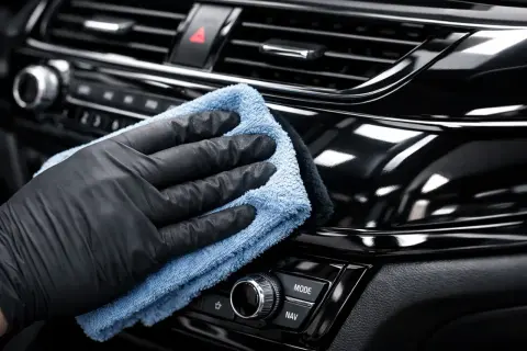 Ręka w czarnej rękawiczce poleruje błyszczące piano black na desce rozdzielczej samochodu, przywracając mu głęboki połysk.