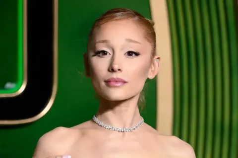 Ariana Grande w błyszczącym naszyjniku, wygląda na zmęczoną, jakby zmagała się z chorobą.