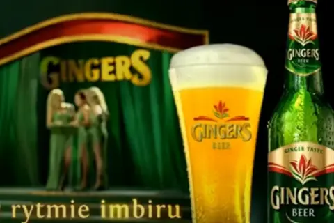 Piwo Gingers: orzeźwiający smak imbiru w szklance i butelce, na scenie z tancerkami.