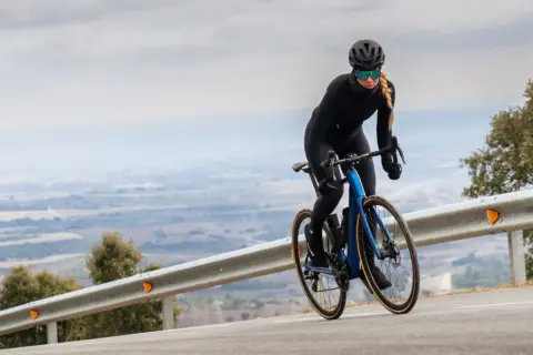 Kobieta w kasku i okularach jedzie na rowerze z niebieskim, aerodynamicznym nadwoziem. Silnik umieszczony centralnie zapewnia moc podczas podjazdu.