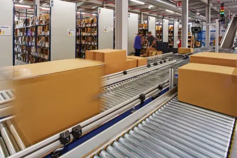 Pudełka na taśmie w magazynie, gotowe do wysyłki. W tle regały z towarem, sugerujące dużą liczbę zamówień i potencjalny **back order**.