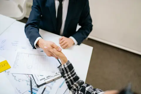 Accordo per vendere immobile: il procuratore valuta i rischi. Due persone si stringono la mano su un tavolo con grafici.