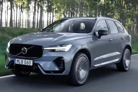 Szary Volvo XC60 z napędem hybrydowym, poruszający się po leśnej drodze. Dostępne różne silniki.