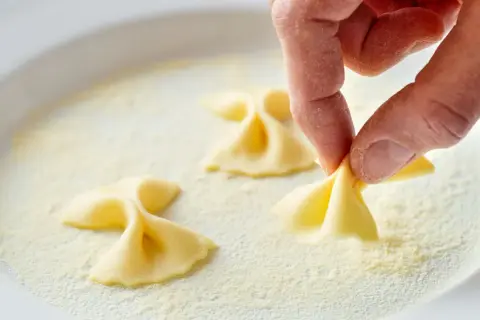 Hand formt Farfalle-Nudeln in einer Schüssel mit Grieß.