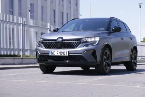 Nowy Renault Austral w matowym, szarym kolorze prezentuje się elegancko na tle nowoczesnego budynku.