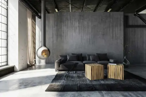 Nowoczesny salon z betonowymi ścianami i podłogą. Centralnym punktem jest wiszący kominek, a obok niego szara kanapa i dwa drewniane stoliki. Surowość formy podkreśla industrialny charakter wnętrza.