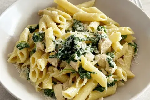 Penne z kurczakiem, szpinakiem i fetą, posypane parmezanem. Pyszne danie, które zachwyci każdego.