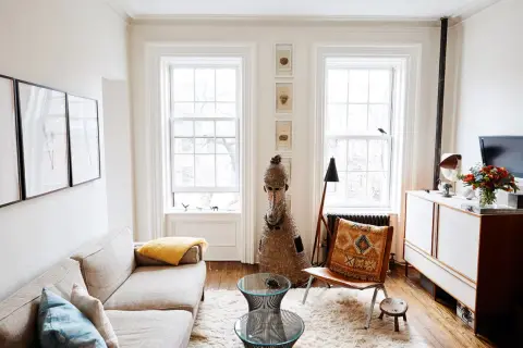 A bright living room with a sofa, fluffy rug, and two windows, demonstrating how to make a small space feel large with light and airy decor.