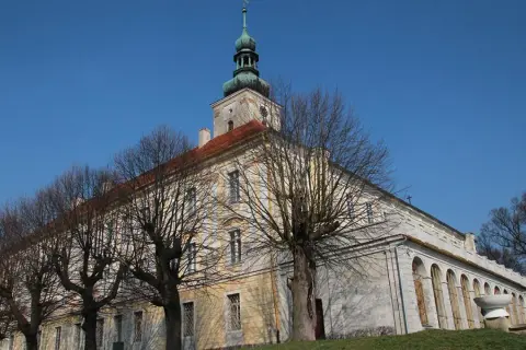Dawny pałac w Oleśnicy Małej z charakterystyczną wieżą i arkadowym krużgankiem, otoczony nagimi drzewami.
