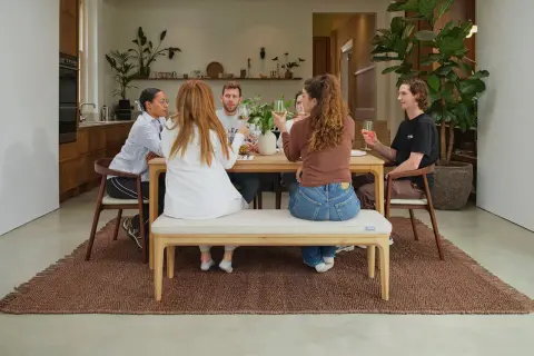 Friends enjoy drinks around a wooden table, showcasing a stylish mix and match of dining chairs and a bench for a relaxed gathering.