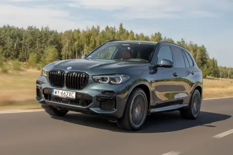 Ciemnozielone BMW X5 45e pędzi po drodze, otoczone zielenią lasów.