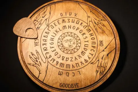 Drewniana plansza Ouija z literami, cyframi i symbolem słońca. Czy to sposób, jak wywołać ducha bez świeczek?