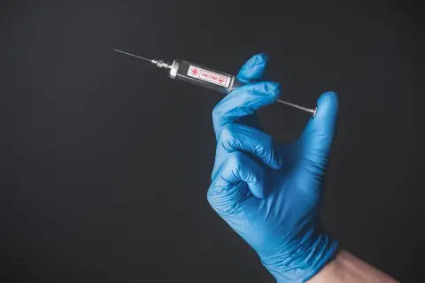 Ręka w niebieskiej rękawiczce trzyma strzykawkę z napisem VACCINE. To symbol szczepień, także w Tunezji.