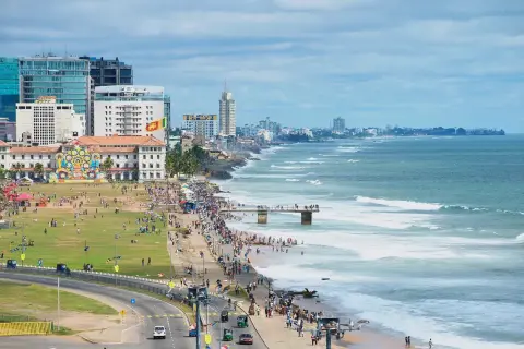 Kolombo, Sri Lanka na własną rękę: tętniące życiem wybrzeże z ludźmi spacerującymi po plaży i zielonym parku, nowoczesne budynki i ocean z falami.